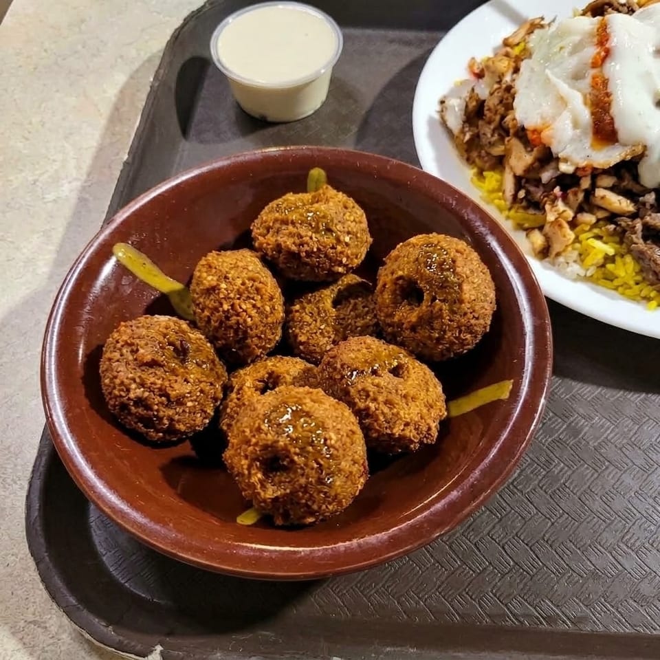 Bowl of golden falafel with pickles, tahini sauce, and a plate of rice topped with chicken and fried eggs.